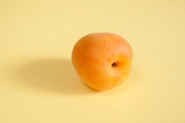 One ripe apricot on pastel yellow background.