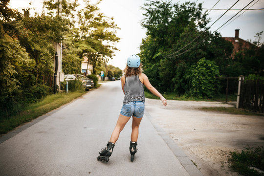 Woman roller skating on city street with helmet on summer from behind