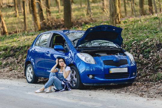 Girl Is Sitting Next To Broken Car With An Open Hood And Speaks By Phone