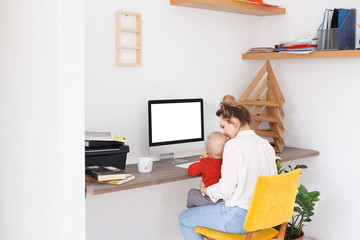 Attractive young pensive mother engineer works remotely at home and engaged in raising a child....