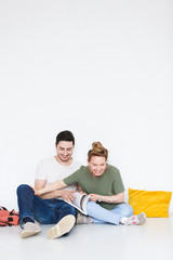 Happy European young man and woman students sitting on floor isolated white wall background. Romantic cute couple enjoys spending studying time together and have fun. Education concept
