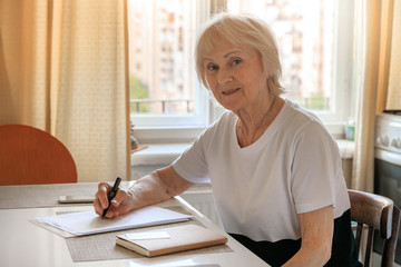 Elderly woman plans her budget, with a notebook, bills and a credit card. Increase in retirement age, savings for a retirement