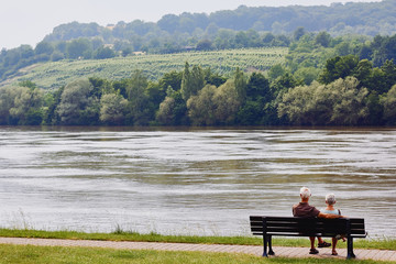 Happy elderly couple is sitting on the bench near the river and taking rest