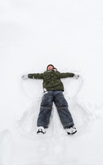 Fototapeta na wymiar Cute little boy lie on white snow. LIttle boy having fun on winter day