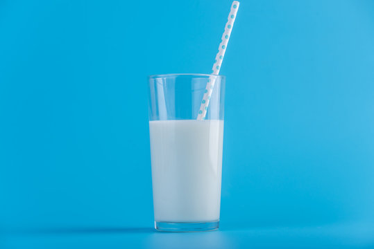Glass of fresh milk with straw on a blue background. Concept of healthy dairy products with calcium