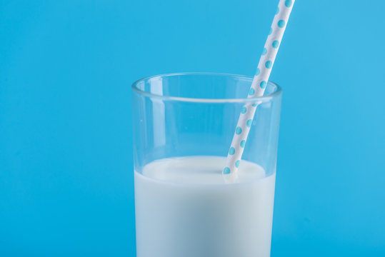 Glass of fresh milk with straw on a blue background. Concept of healthy dairy products with calcium