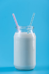 Glass bottle of fresh milk with two straws on blue background. Colorful minimalism. Healthy dairy products with calcium