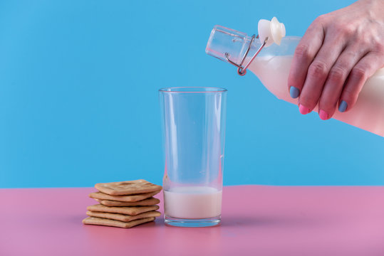 Woman's hand pours fresh milk from bottle into a glass and cookies on a pastel background. Healthy dairy products