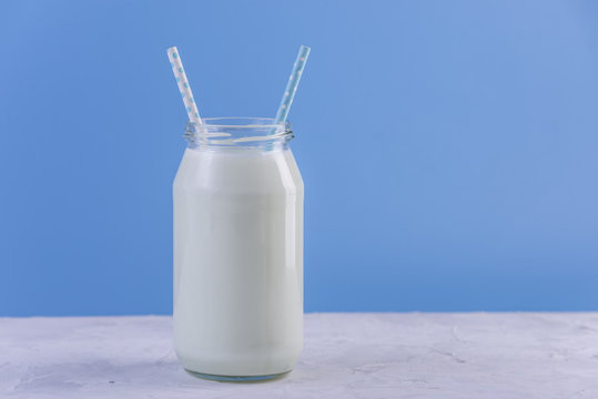 Glass bottle of fresh milk with two straws on blue background. Colorful minimalism. Healthy dairy products