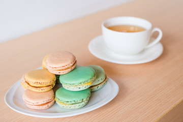 Sweet and colorful French macaroons dessert with a cup of green tea background on wooden table