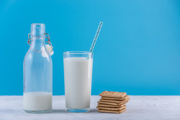 Bottle of fresh milk with straw and cookies on blue background. Colorful minimalism. Healthy dairy products with calcium