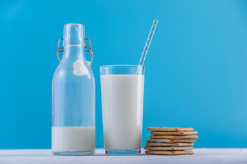 Bottle of fresh milk with straw and cookies on blue background. Colorful minimalism. Healthy dairy products with calcium