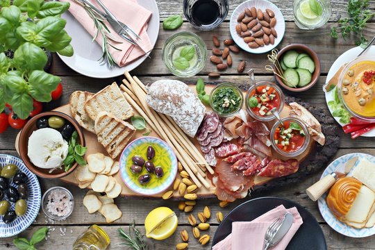 
    Mediterranean appetizers table concept. Dinner table with tapas selection: cured meat and salami, gazpacho soup, jamon, olives, cheese, hummus and vegetables. Overhead view.