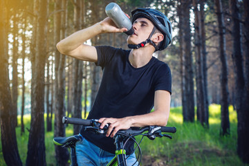 Obraz premium Cyclist in a helmet drinking water from a bottle while riding in the Park. Concept of active and healthy lifestyle
