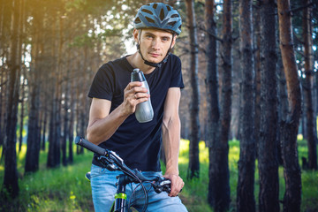 Cyclist in a helmet drinking water from a bottle while riding in the Park. Active and healthy lifestyle