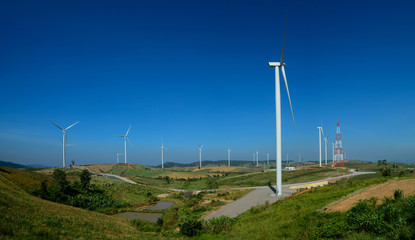 Windmills farm or Wind turbine power generators standing on green mountain against a blue sky,...