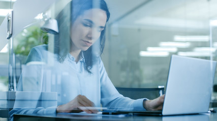 In the Office Beautiful Accountant Works on the Laptop and Smiles. Modern Glass and Concrete Room.