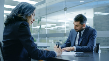 Businesswoman and Businessman Have Conversation. Sign Documents, Draw up a Contract, Seal the Deal, Finish Transaction, Come to an Agreement. They're in Modern Conference Room.