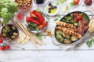  Grilled meat, chicken skewers and sausage  with roasted vegetables and appetizers variety serving on party outdoor table. Mediterranean dinner table concept. Overhead view. © losangela