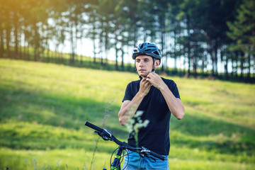 Cyclist is wearing a sports helmet on his head in the background of green nature. Concept of...