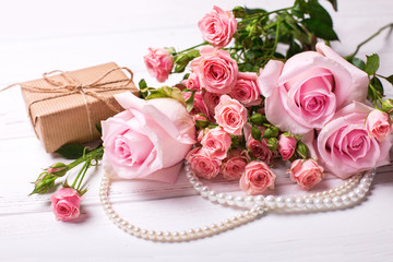 Fresh pink roses flowers  and  wrapped box with present on white wooden background.
