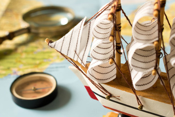 Model sailboat, compass and magnifying glass on map background. Travel concept