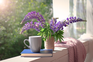 Delicate composition with purple lupines bouquet, cup and book
