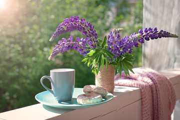 Delicate composition with purple lupines bouquet, cup and cakes