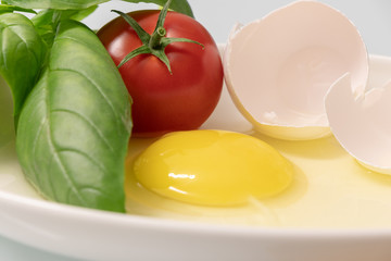 red tomato, basil and egg yolk on a white plate