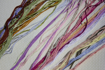colorful strands of floss lying on a white canvas diagonally
