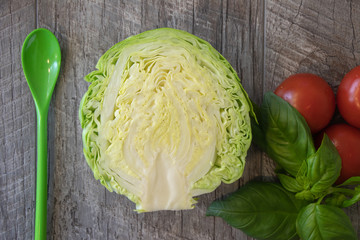 red tomatoes, basil, green spoon and young cabbage in a cut on a wooden table