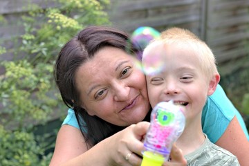 Defect,childcare,medicine and people concept- happy mother and son with down syndrome playing in a garden.