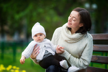 Portrait of happy mom playing with a smiling baby girl outdoors at green park background. Concept of happy family.