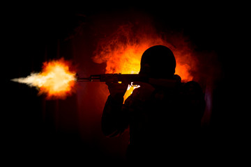 Silhouette of man with assault rifle ready to attack on dark toned foggy background or dangerous...