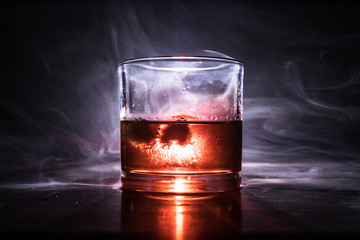 Glass of whiskey and ice on wooden surface with color light and fog on background. Copy space....