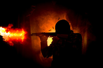 Silhouette of man with assault rifle ready to attack on dark toned foggy background or dangerous...
