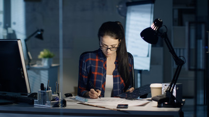 Late at Night Female Solar Engineer Works on Drafts, Holds Part of Solar Panel and Uses Her...