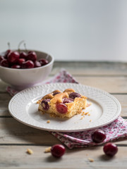 Cherry sponge cake and white ceramic bowl of fresh cherries on white rustic wooden table.
