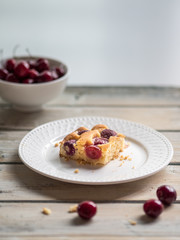 Cherry sponge cake and white ceramic bowl of fresh cherries on white rustic wooden table.