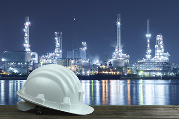 Industry background with helmet of worker and Oil refinery at background.