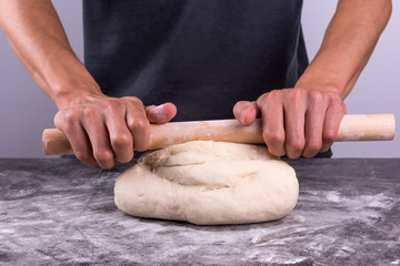 Dough with flour, rolling pin. Male hands rolling out dough on the table.