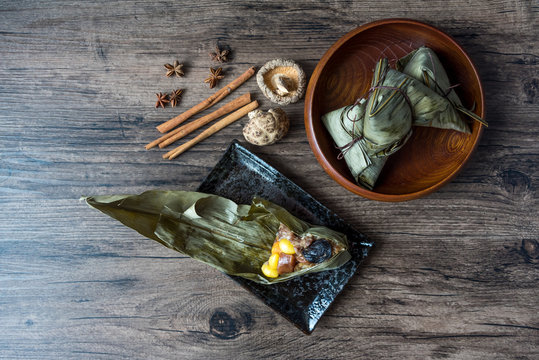 Zongzi or Traditional Chinese Sticky Rice Dumplings made of glutinous rice stuffed with different fillings and wrapped in bamboo reed (or other large flat leaves) on wood table.