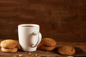 White porcelain mug of tea and sweet cookies on piece of wood over wooden background, top view, selective focus