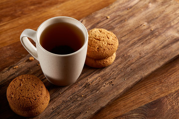 White porcelain mug of tea and sweet cookies on piece of wood over wooden background, top view, selective focus