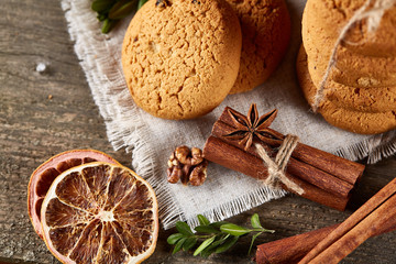 Christmas composition with pile of cookies, cinnamon and dried oranges on light wooden background, close-up.