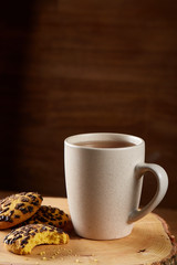 White cup of tea and cookies on a log over country style wooden background, close-up, selective focus