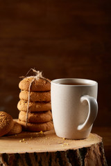 Christmas concept with a cup of hot tea, cookies and decorations on a log over wooden background, selective focus