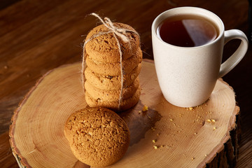 Christmas concept with a cup of hot tea, cookies and decorations on a log over wooden background, selective focus
