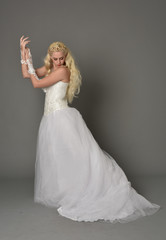 Naklejka premium full length portrait of blonde girl wearing white fantasy gown. standing pose in side profile, grey studio background.