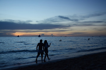Sunset time at a beautiful island with orange gradient colour of sky and people playing around the beach.